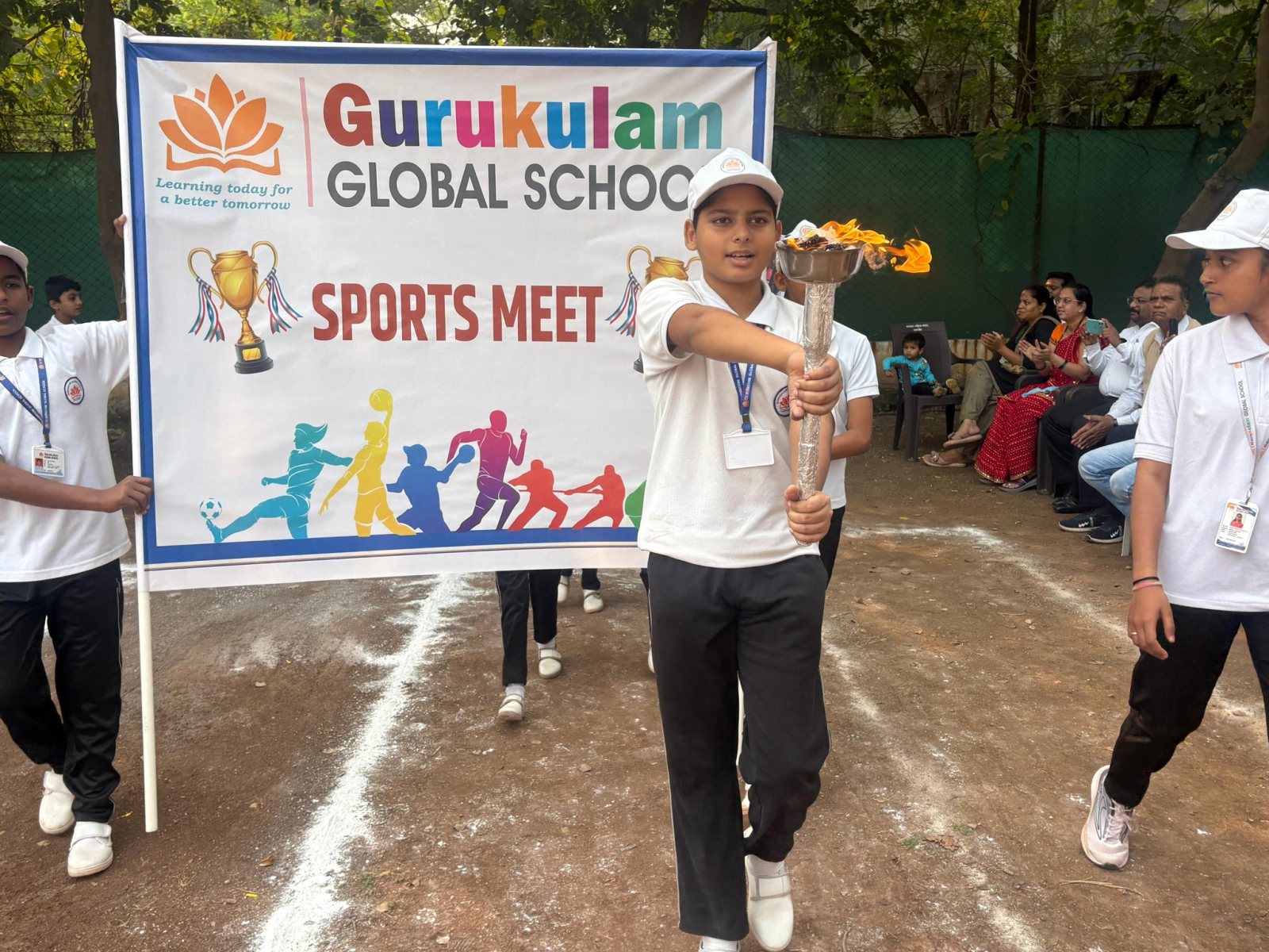 The torch bearer leads the Sports Meet banner onto the ground
