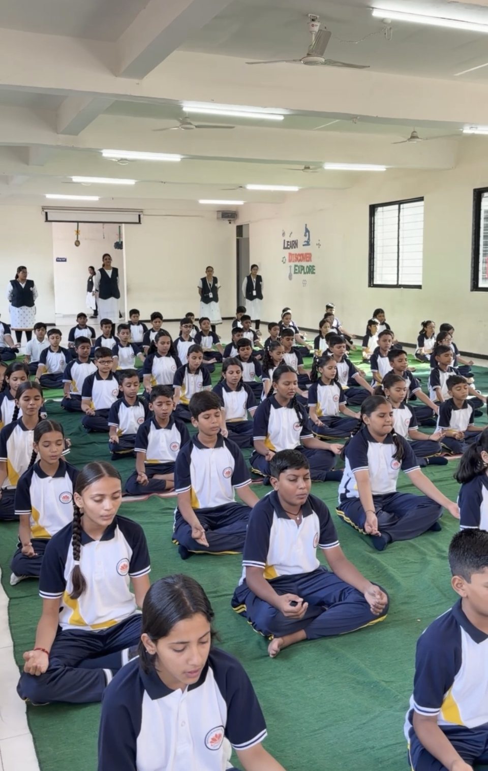 Rows of students in sukhasana in the hall